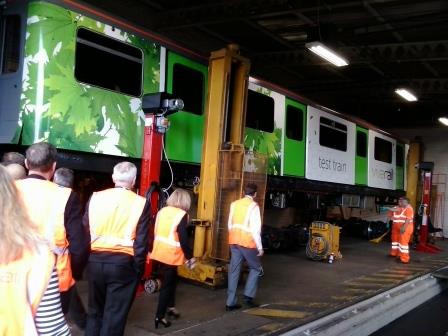 Invited guests take a look under the Vivarail D-Train that has been lifted up by jacks in the depot
